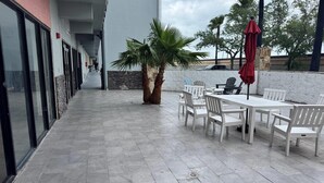 Un patio al aire libre con una mesa, sillas, una palmera y un paraguas rojo.