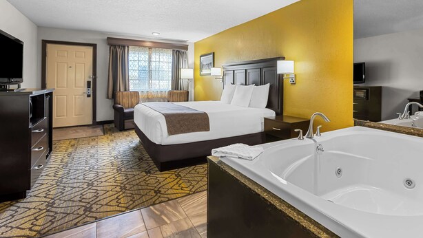 A hotel room with a large bed, a separate bathroom with a bathtub, a television, and a desk with a chair. - Best Western of Harbor Springs (Harbor Springs)