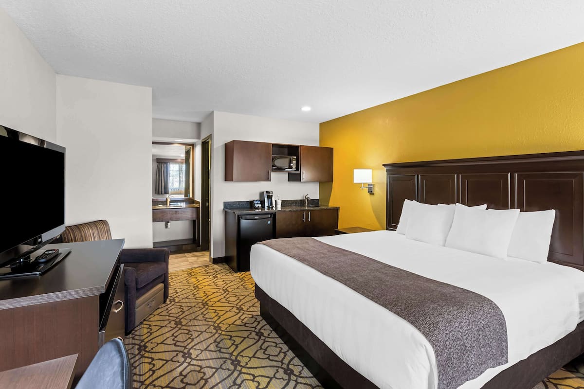 A hotel room with a large bed, a desk with a TV, a microwave, and a small kitchenette.