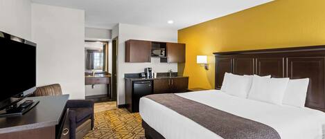 A hotel room with a large bed, a desk with a TV, a microwave, and a small kitchenette.
