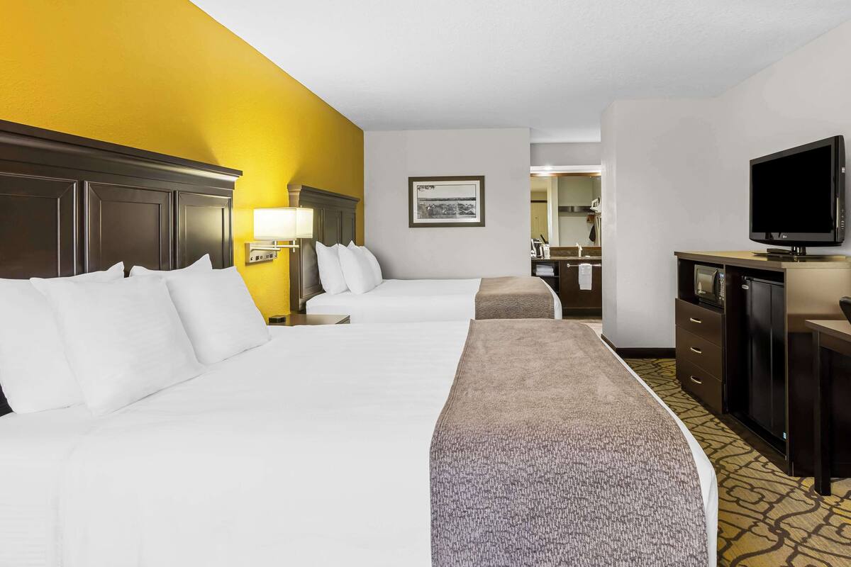 A hotel room with two beds, a television, a desk, and a bathroom visible in the background.