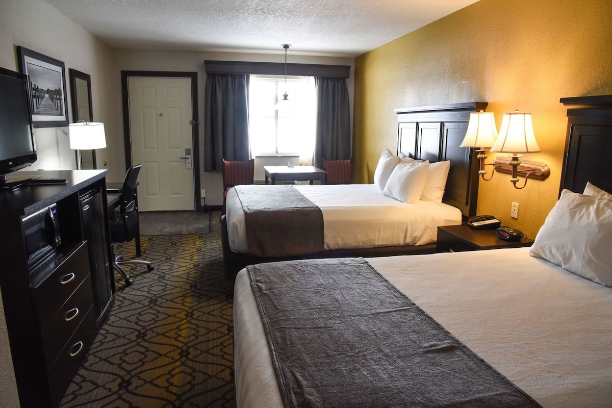 A hotel room with two beds, a desk, a chair, a desk lamp, and a clock.