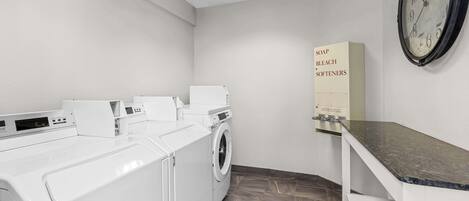A laundry room with a washing machine, dryer, and a shelf with a box labeled "SOAP BLEACH SOFTENERS".