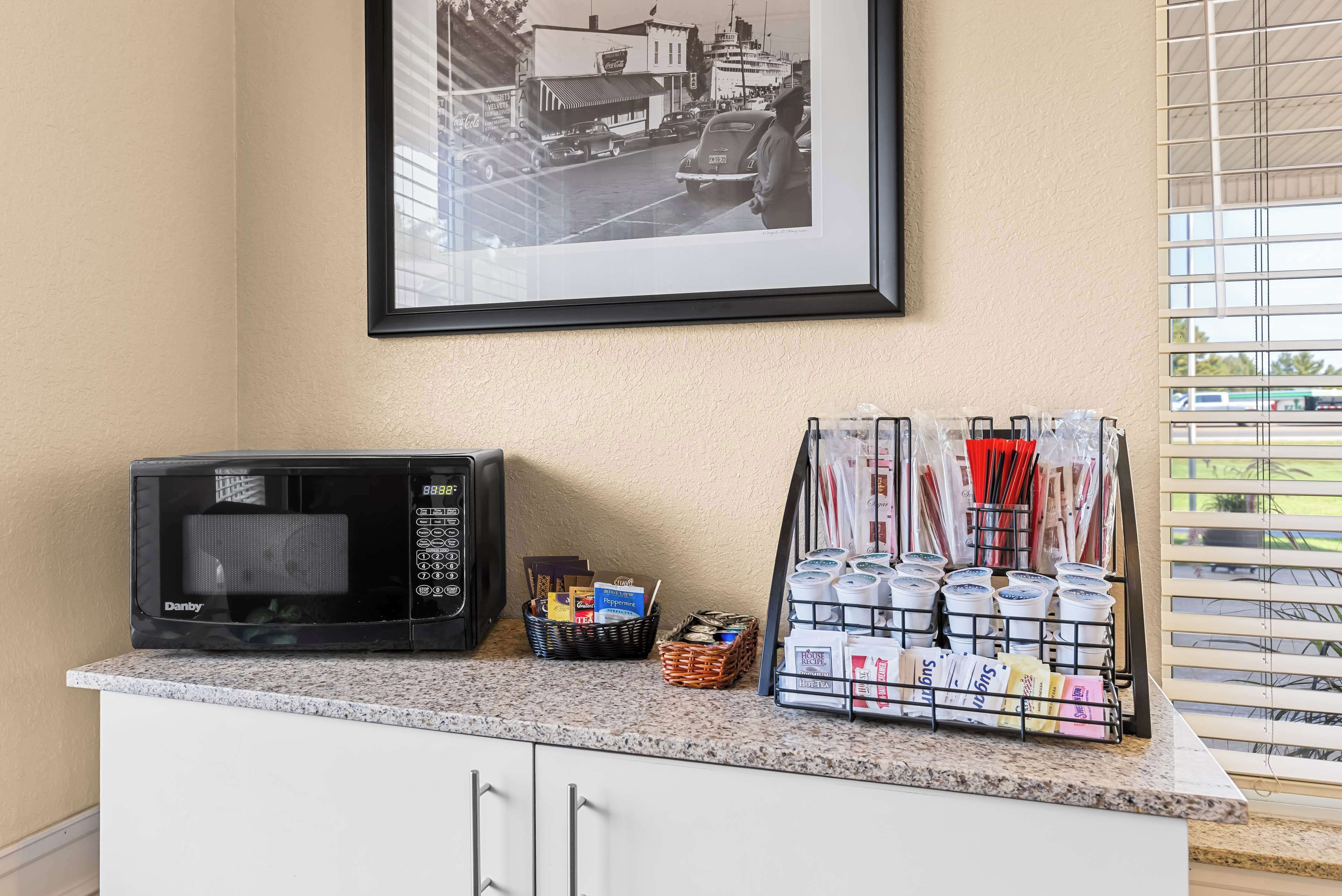 A kitchen counter with a microwave, a basket of books, and a rack of coffee cups.