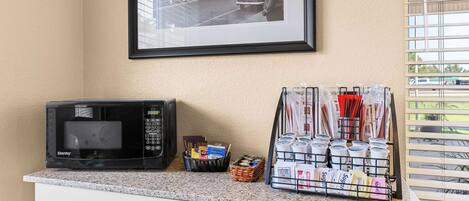 A kitchen counter with a microwave, a basket of books, and a rack of coffee cups.