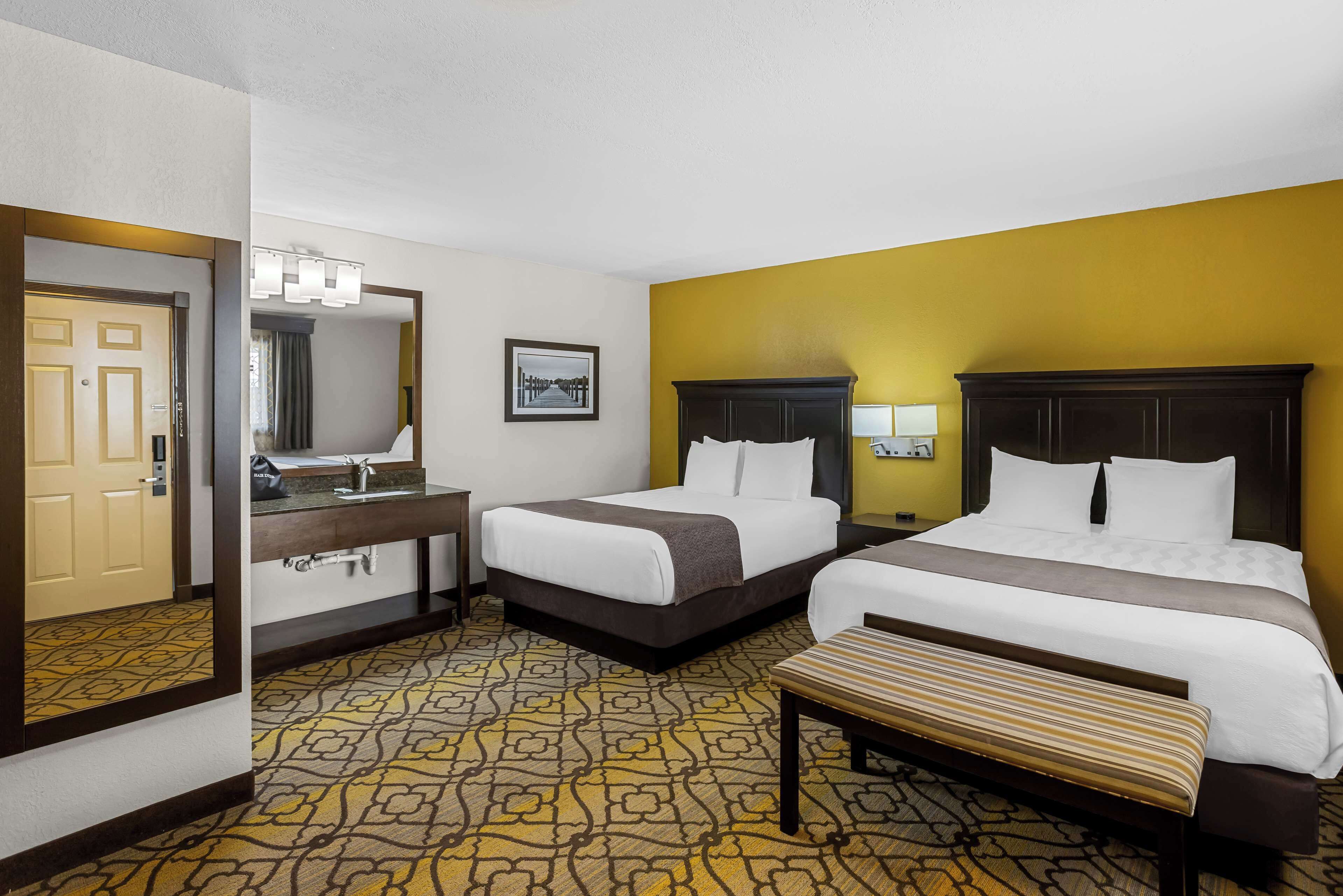 A hotel room with two beds, a large mirror, a bathroom with a sink, and a patterned carpet.