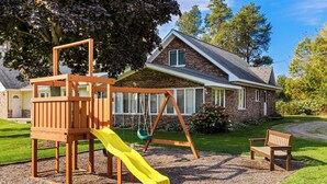 A playground with a slide and swings, a bench, and a house in the background. - Best Western of Harbor Springs (Harbor Springs)