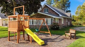 Enjoy a serene outdoor play area with a play structure and swing set, adjacent to a two-story house with large windows.