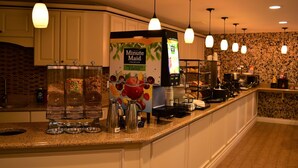 A breakfast bar with a fruit juice dispenser, coffee maker, and stacked plates. - Best Western of Harbor Springs (Harbor Springs)