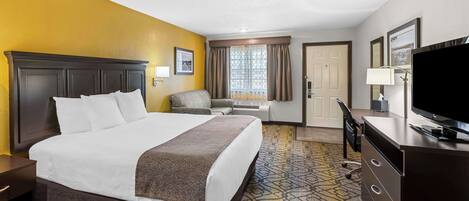 A hotel room with a large bed, a desk, a television, and a window with curtains.