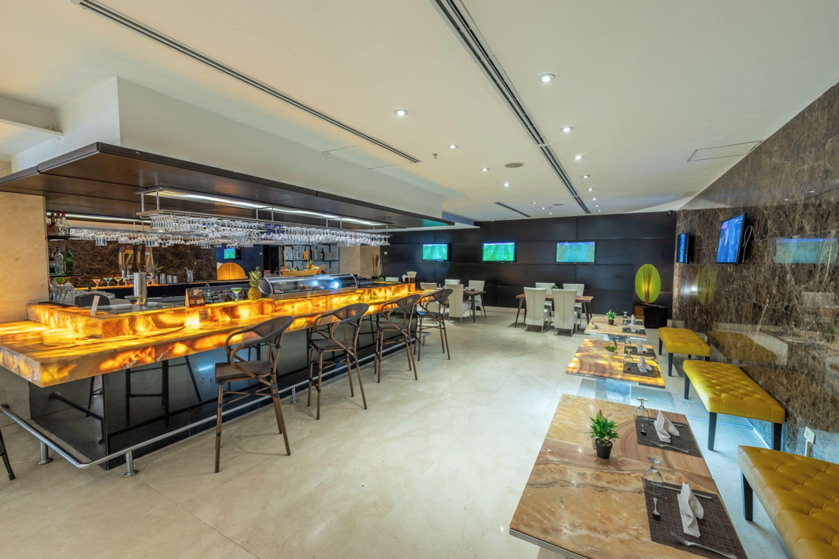 A modern bar area with a long counter, bar stools, and a seating area with tables and chairs.