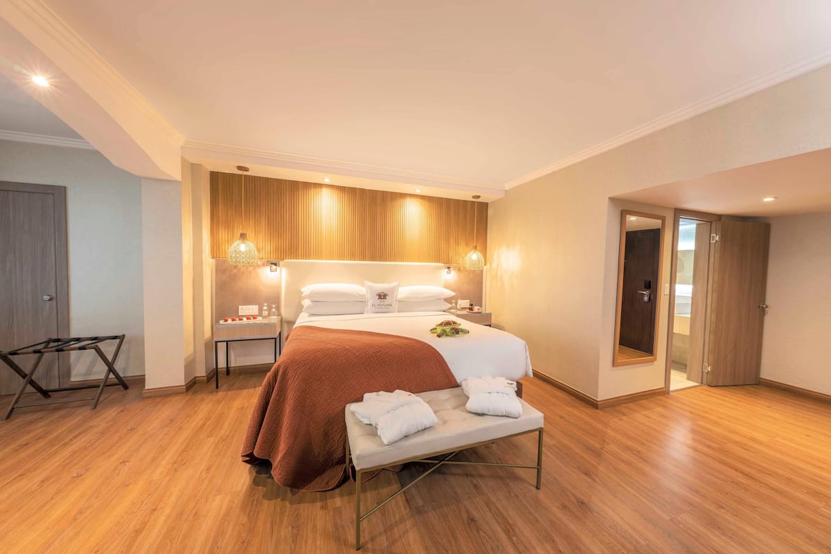 Habitación de hotel con una cama grande, mesitas de noche, un banco con toallas y suelo de madera.
