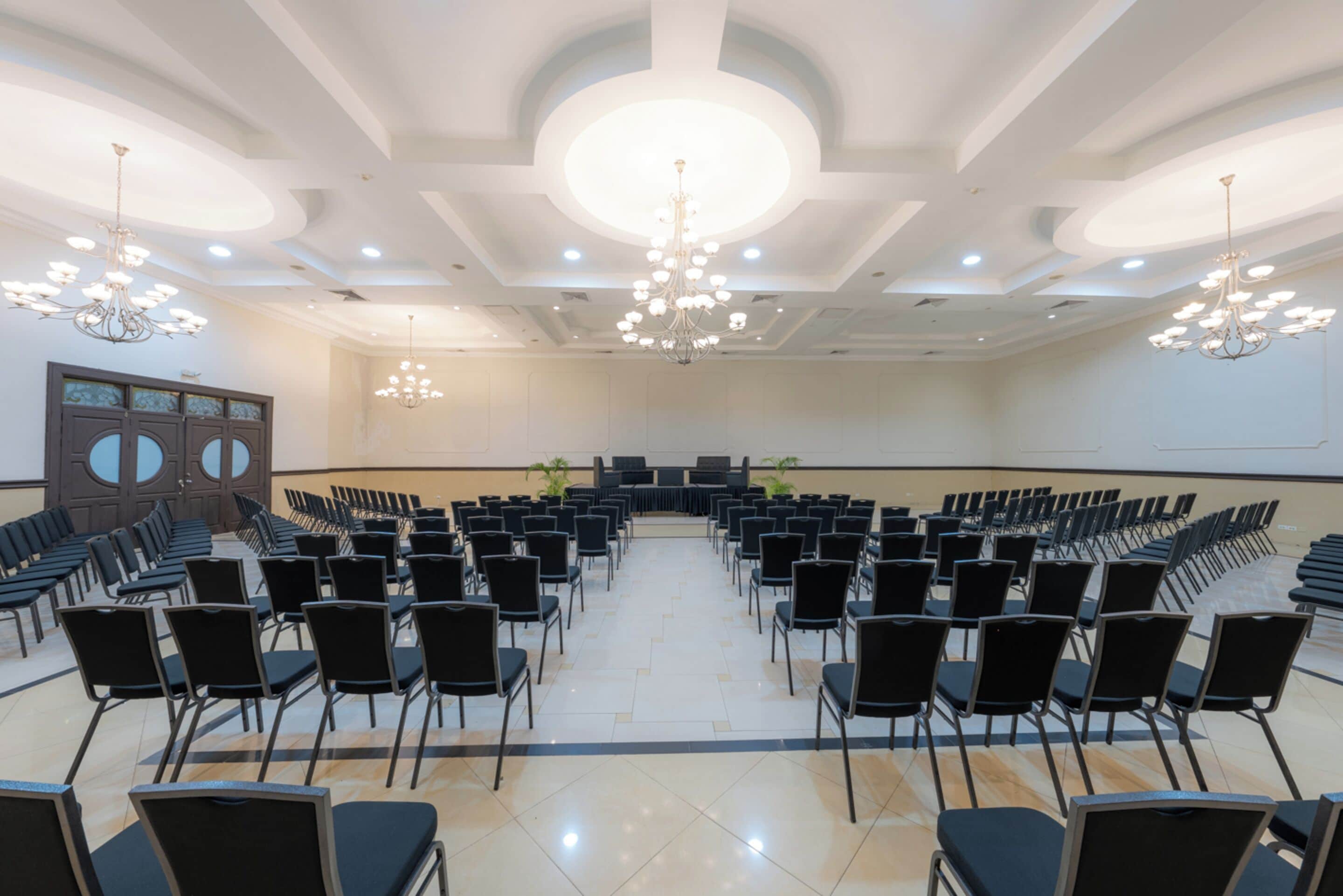 Une salle de conférence avec des rangées de chaises, une scène et des lustres.