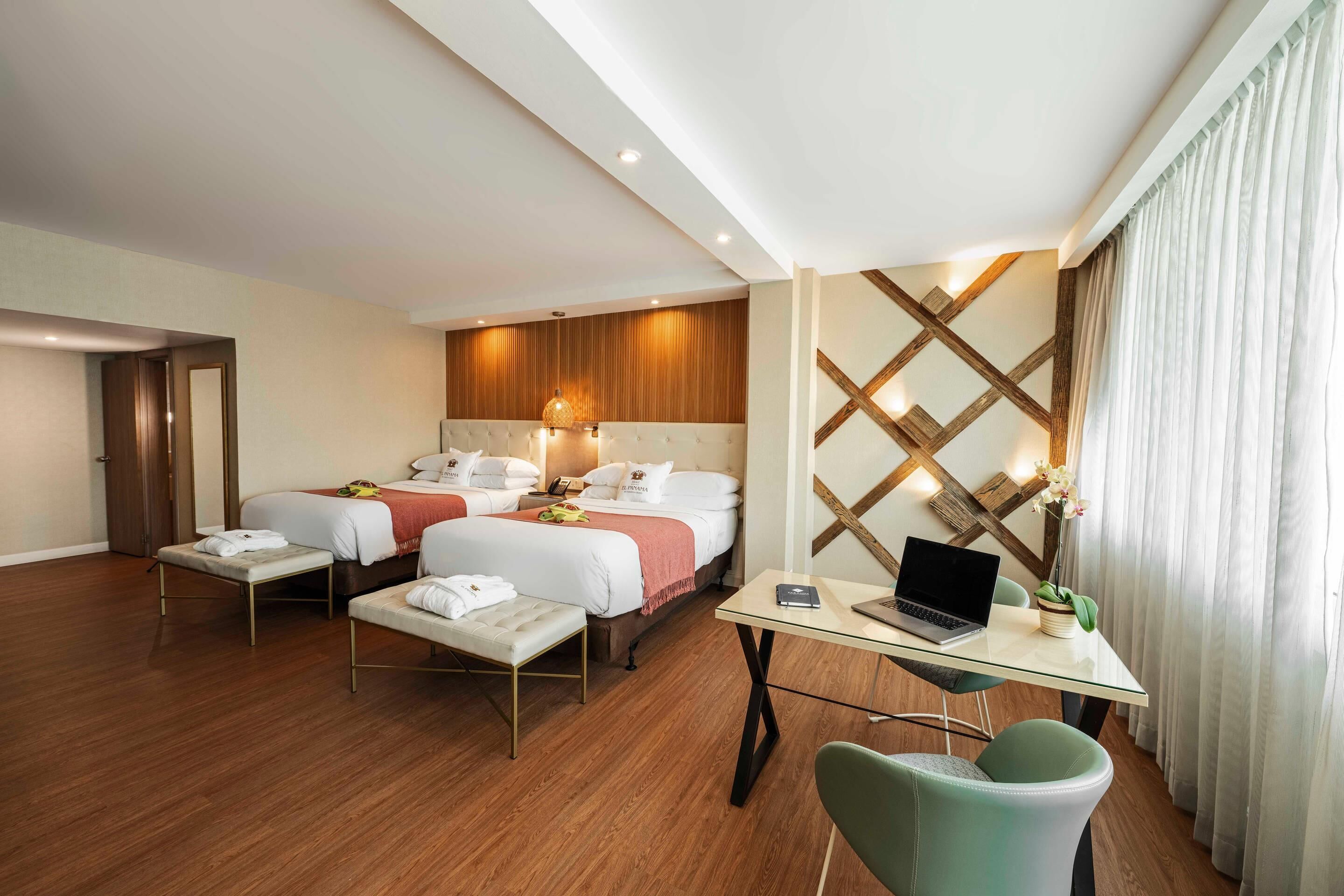 A hotel room with two beds, a desk with a laptop, a chair, and a small table with a plant.