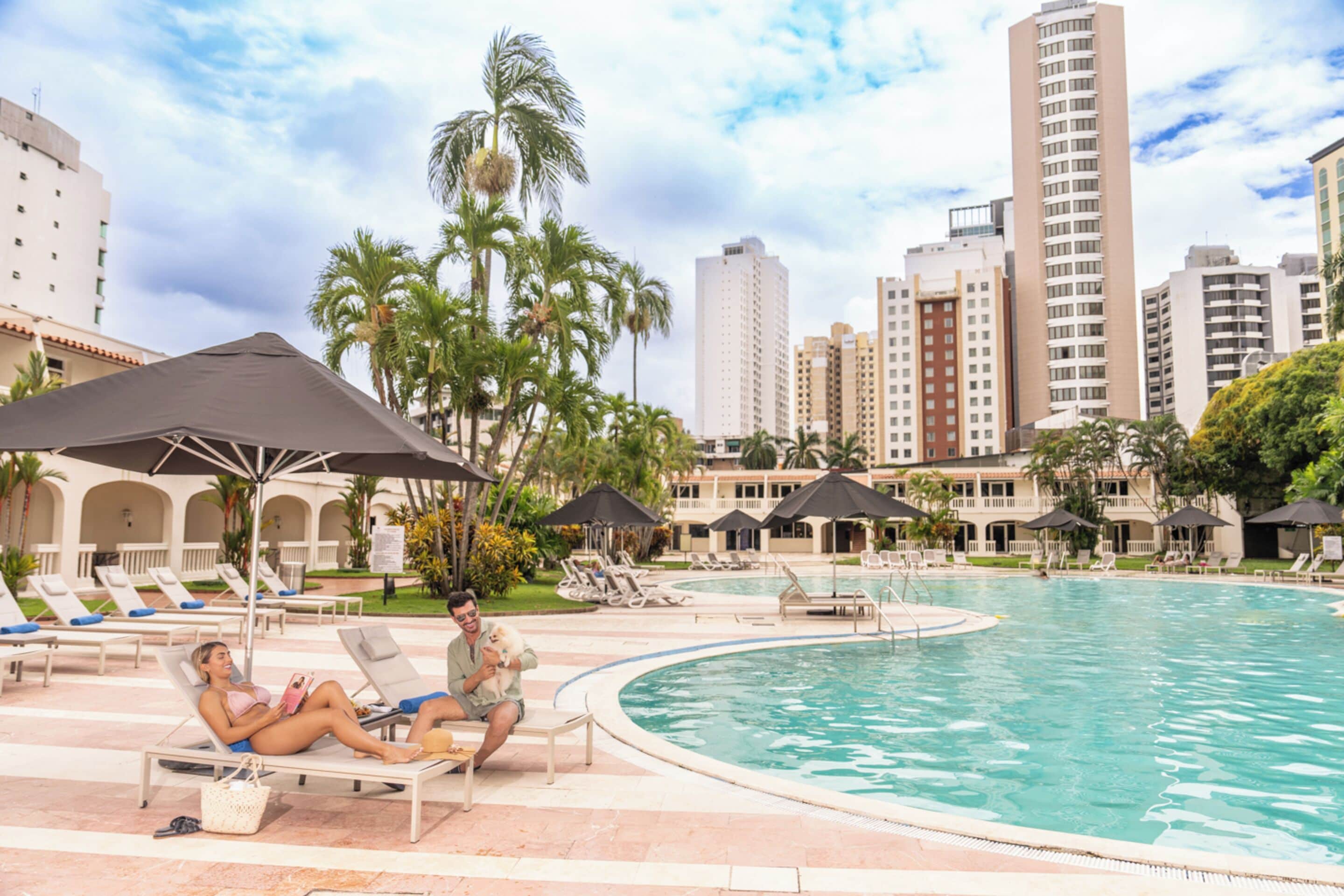A poolside area with lounge chairs, umbrellas, and a clear view of tall buildings in the background.