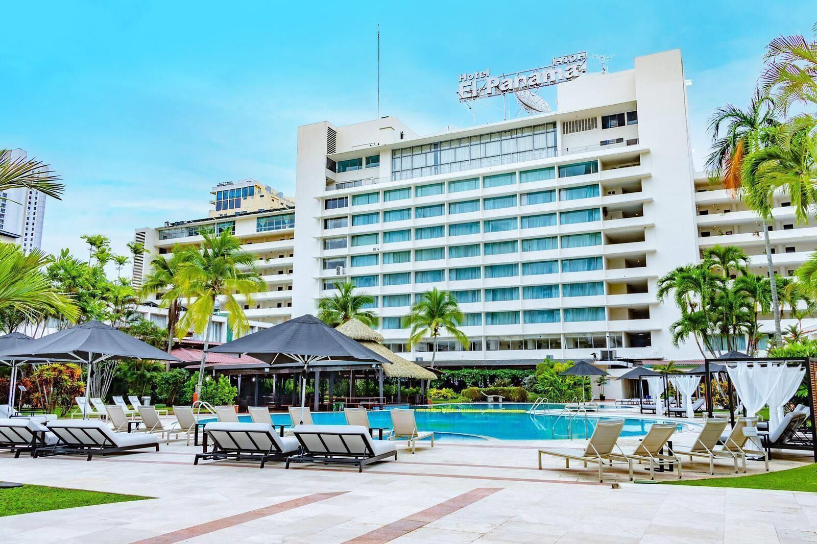Un hotel con una piscina amplia, varios balcones y palmeras.
