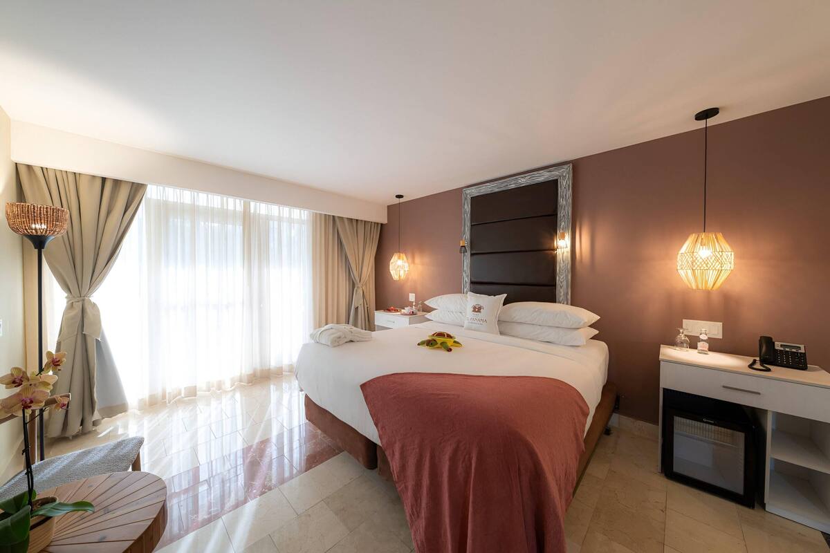 Quarto de hotel com cama, mesa de cabeceira, luminária e um pequeno frigorífico.