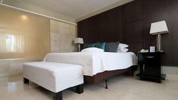 Habitación de hotel con cama, mesitas de noche, un banco y una ventana con cortinas.