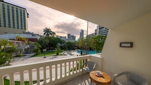 A balcony with a view of a swimming pool, palm trees, and city buildings.
