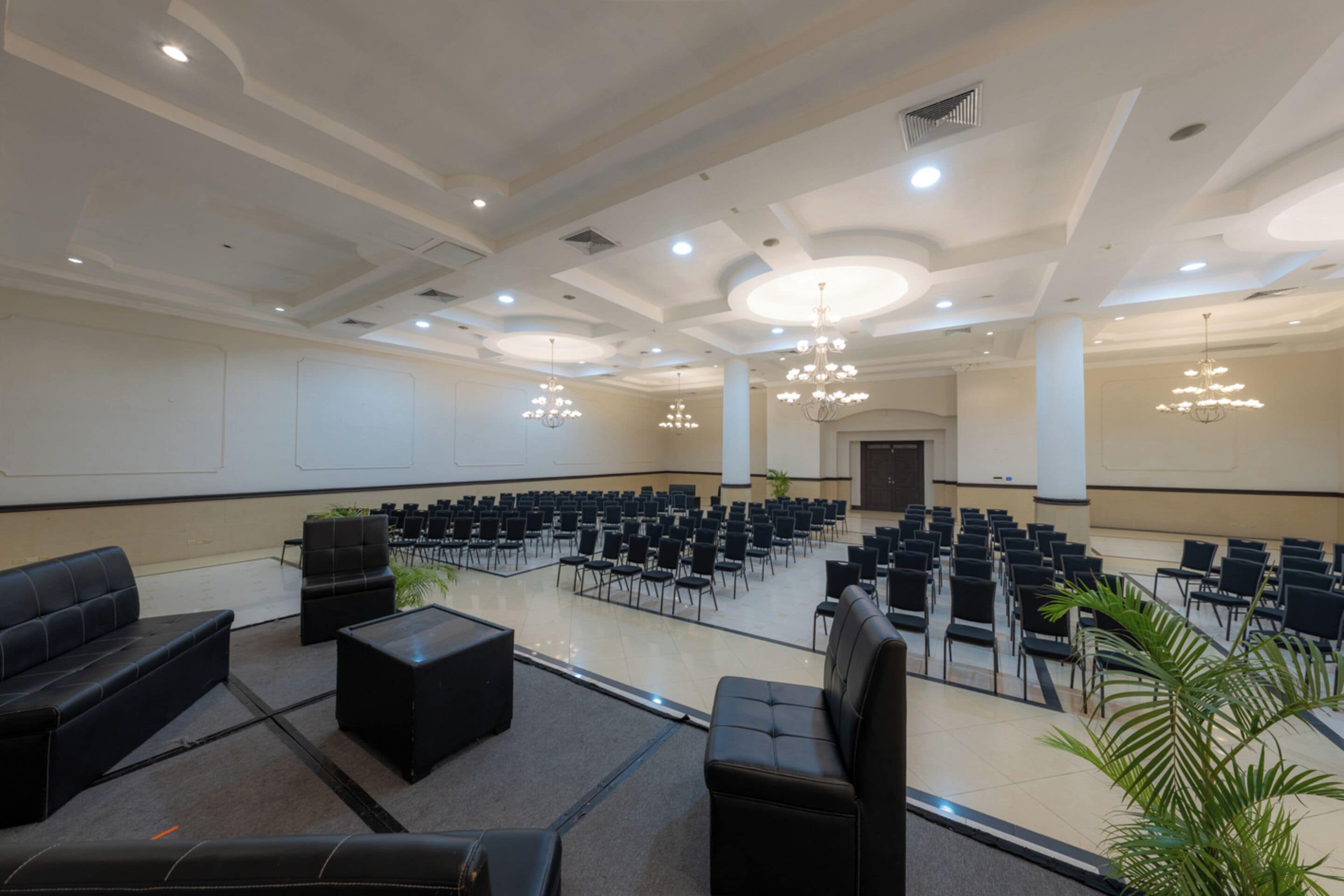 Un salón de conferencias con filas de sillas, un escenario y una zona de estar con sofás y mesas.