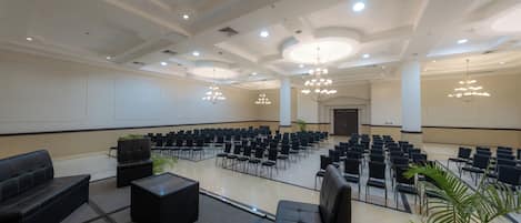 Un salón de conferencias con filas de sillas, un escenario y una zona de estar con sofás y mesas.