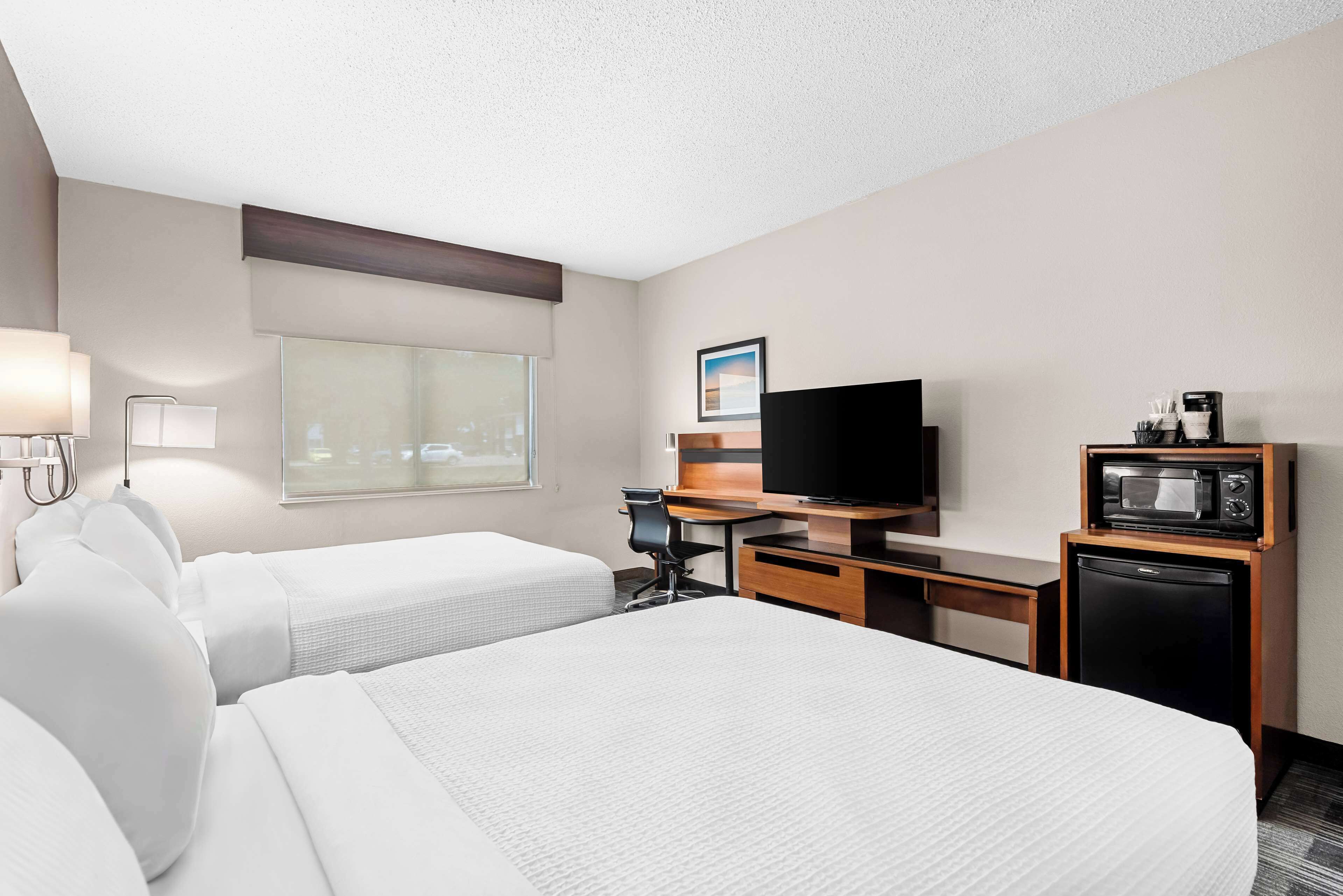 Habitación de hotel con dos camas, un escritorio, televisión, microondas y ventana con vistas.