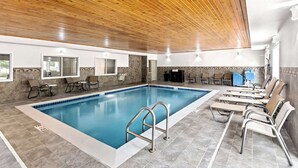 Una piscina interior con techo de madera, sillas de descanso y suelo de baldosas.