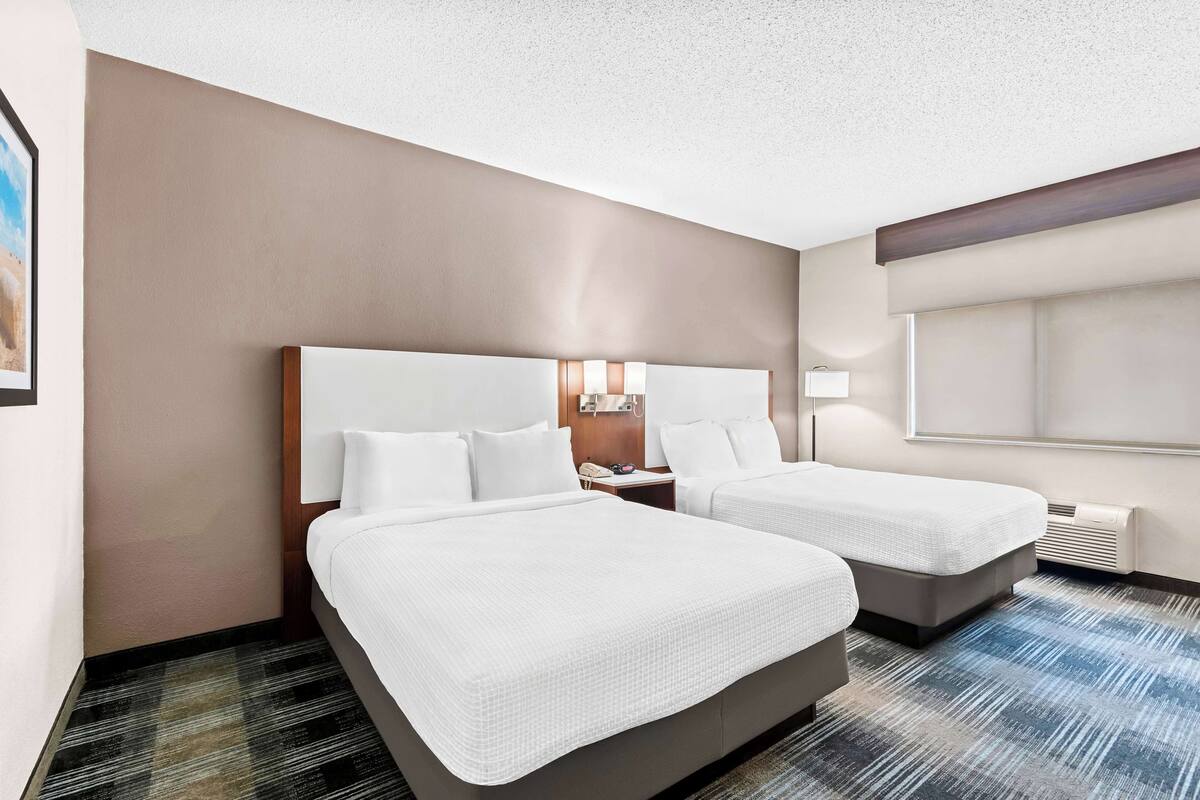 Une chambre d’hôtel avec deux lits, une table de chevet, une lampe et une fenêtre.
