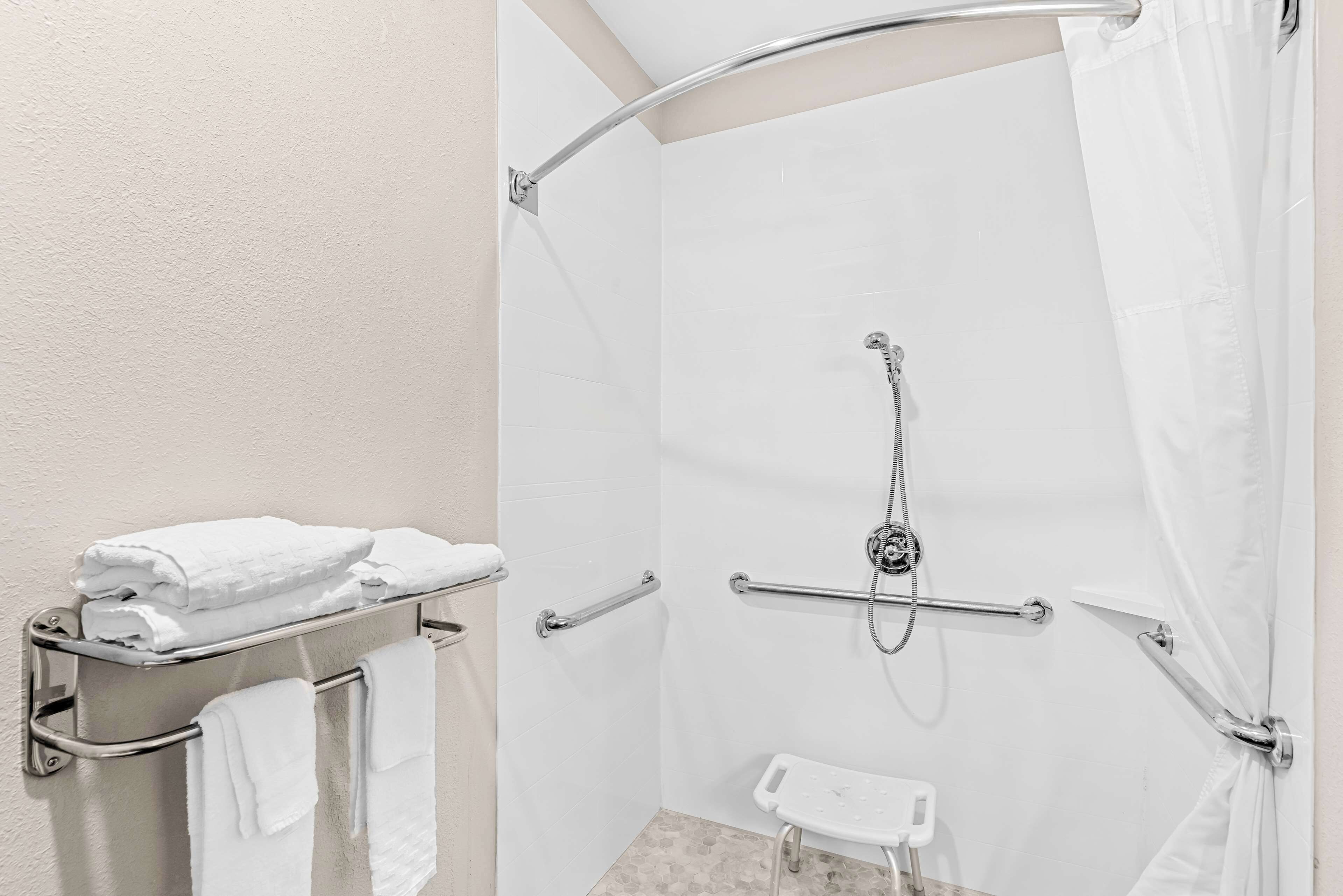 Zona de ducha con barra de apoyo, cortina de ducha blanca y toallero con toallas dobladas.