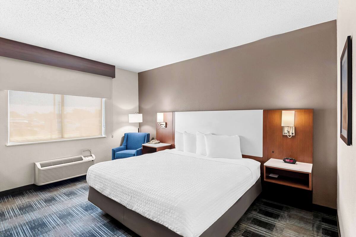 Une chambre d’hôtel avec un grand lit, un bureau avec une lampe, une chaise, une table de chevet et une fenêtre donnant sur un beau paysage.