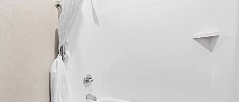 Una bañera blanca con cortina de ducha y ducha de mano.