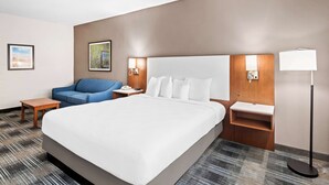 Una habitación de hotel con una cama grande, un sofá azul, una mesita de noche con una lámpara y una pequeña mesa.