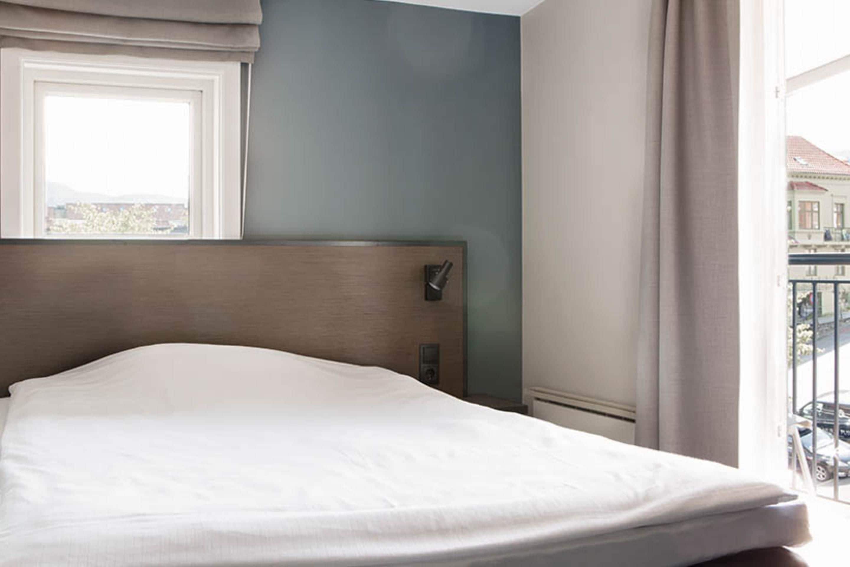 A neatly made bed in a hotel room with a view of the city through a window.