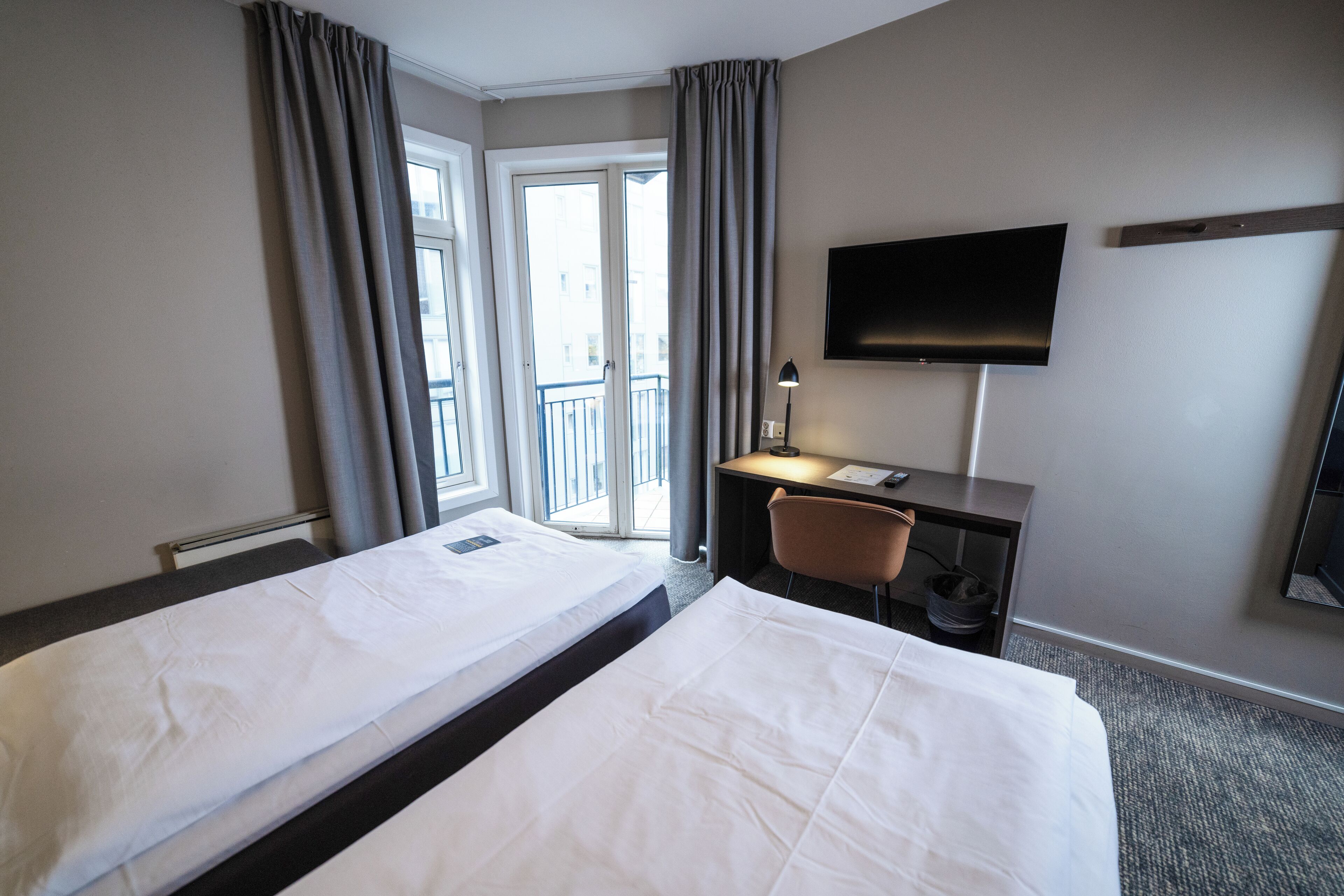 Hotellihuone, jossa on kaksi sänkyä, työpöytä, tuoli, televisio ja parveke.