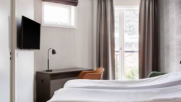 Une chambre d’hôtel avec un lit, un bureau, une chaise, une télévision et une fenêtre avec des rideaux.