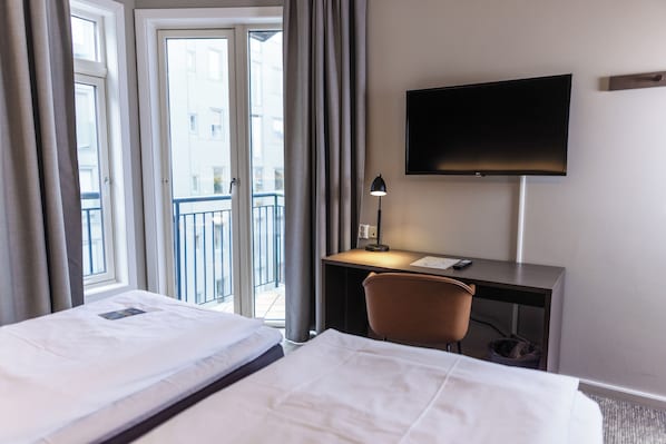 Habitación de hotel con cama, escritorio, silla, televisor y ventana con cortinas.