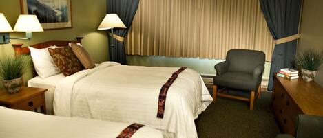 A hotel room with two beds, a chair, a desk, and a window with curtains.