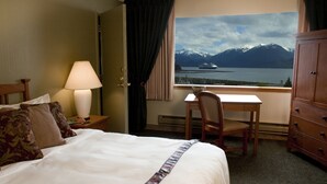 Une chambre d’hôtel équipée d’un lit, d’un bureau, d’une chaise, d’une lampe, d’une commode et d’une fenêtre donnant sur la montagne et le lac.