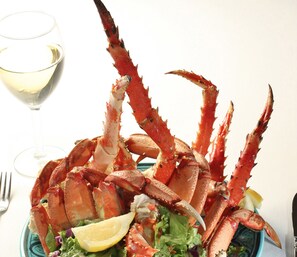 Un plato de patas de cangrejo cocidas con una cuña de limón y una copa de vino blanco al lado.