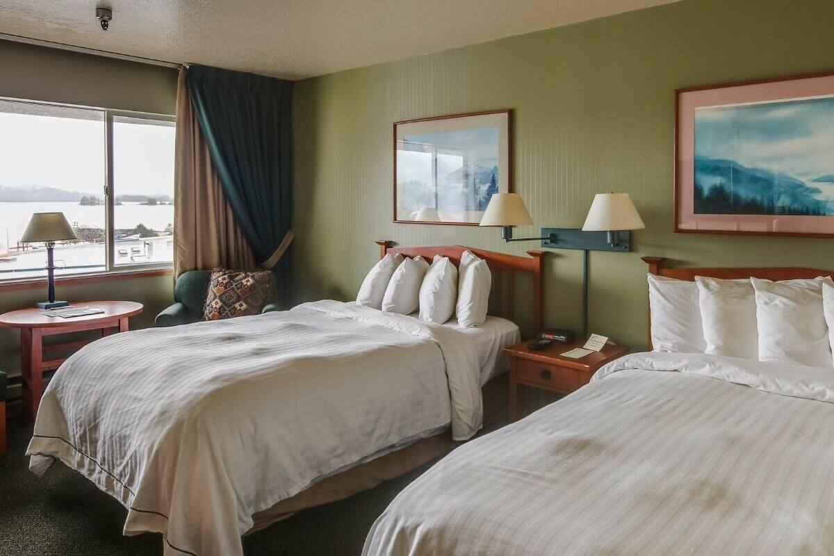Une chambre d’hôtel avec deux lits, un bureau, une chaise et une fenêtre donnant sur l’eau.