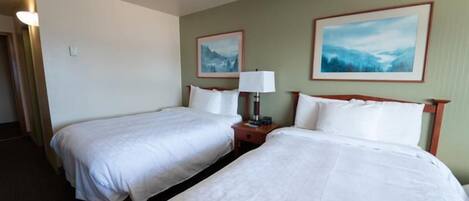 Quarto de hotel com duas camas, uma mesa de cabeceira, um abajur e dois quadros na parede.
