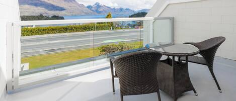 A balcony with wicker chairs and a glass table overlooking a road and mountains.