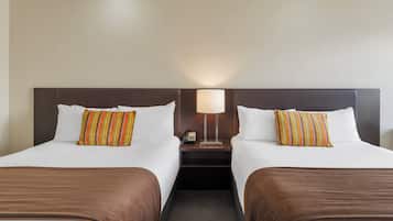 A hotel room with two beds, each with a brown bedspread and striped pillows. There is a nightstand with a lamp and a phone between the beds.