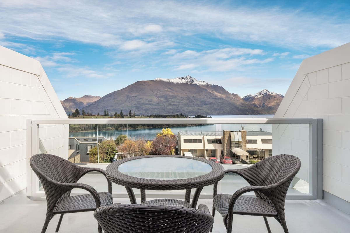 Un balcon doté de meubles en osier et d’une table en verre, offrant une vue sur une montagne et un lac.