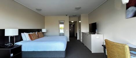 A hotel room with a bed, bedside table, lamp, desk, chair, and a television.