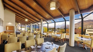 A restaurant with wooden ceiling beams, large windows with mountain views, and neatly arranged tables and chairs.