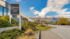 A hotel sign with "Cophorne Hotel & Apartments Queenstown Lakeview" and a view of mountains in the background.