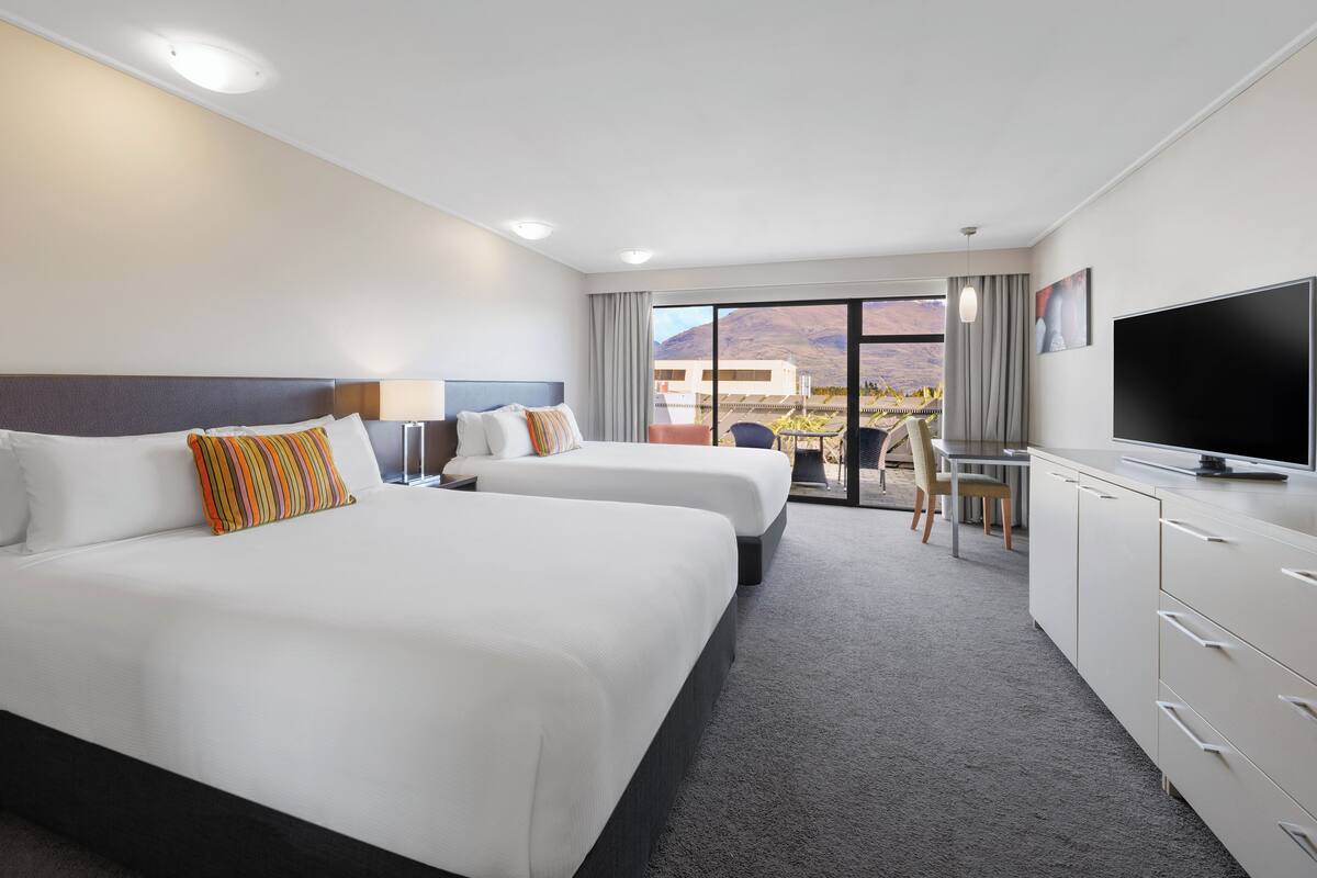 Une chambre d’hôtel avec deux lits, un bureau, une télévision et une vue sur les montagnes.