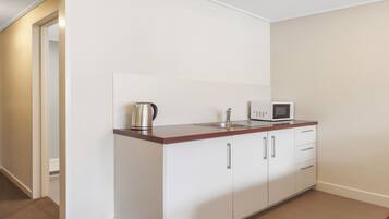A small kitchenette with white cabinets, a stainless steel kettle, a microwave, and a sink.