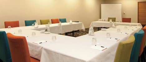 A conference room with white tables, colorful chairs, and water pitchers.